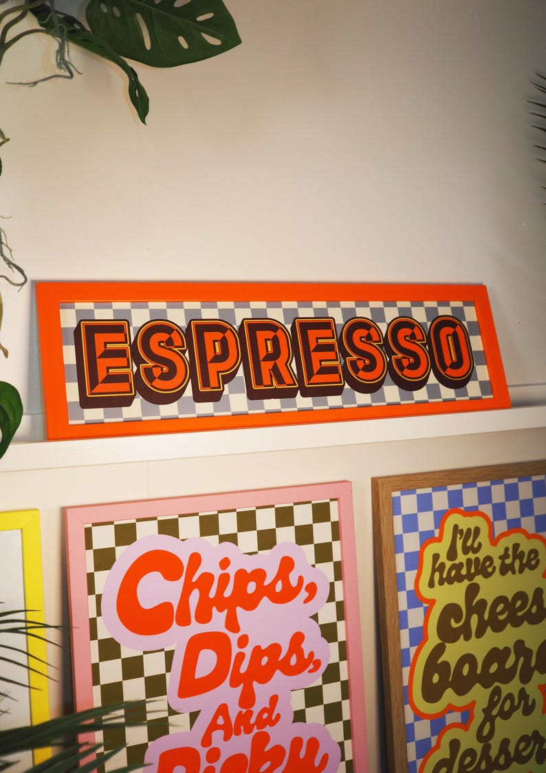 May include: A framed sign with the word "ESPRESSO" in orange, retro-style lettering. The sign has a checkered background and an orange border. Other framed signs with text are visible below.