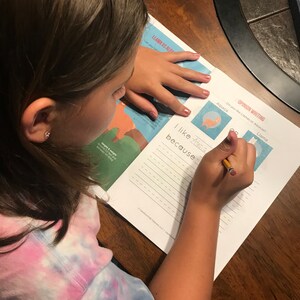 May include: A child writing on a worksheet with the text "Llama vs Alpaca" and "Opinion Writing". The child is wearing a tie-dye shirt and using a pencil to write. The worksheet includes the text "I like Alpaca because".