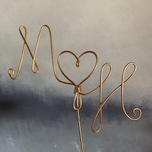 May include: Gold wire sculpture of the letters "M & H" with a heart in the middle.