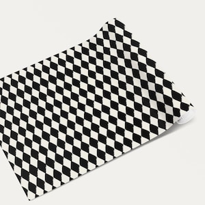 Pode incluir: Um tecido parcialmente enrolado com um padrão de losangos em preto e branco. O tecido é de cor neutra e o padrão de losangos é uniformemente espaçado. O tecido é provavelmente usado para decoração de casa ou projetos de artesanato.