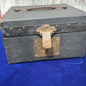 May include: A vintage black trunk with a leather handle and metal hardware. The trunk features a brass lock and rivets along the edges. The exterior shows signs of wear, adding to its antique charm. The trunk is likely used for storage or travel.