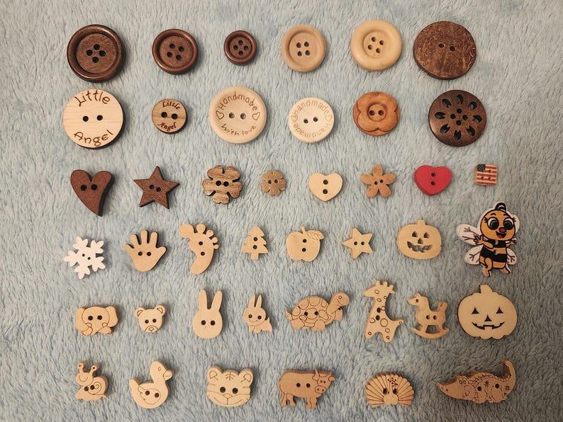 Op de afbeelding: Een verzameling houten knopen in verschillende vormen en maten. Bevat ronde knopen in bruine tinten en decoratieve knopen met hart-, ster- en diermotieven. Sommige knopen hebben de tekst "Little Angel" en "Handmade with love".