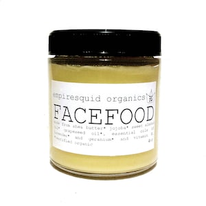 May include: A clear glass jar with a black lid, filled with a pale yellow cream. The label reads "FACEFOOD" and lists ingredients like shea butter and jojoba oil. The jar contains 4 oz of product.