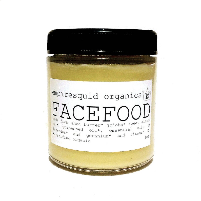 May include: A clear glass jar with a black lid, filled with a pale yellow cream. The label reads "FACEFOOD" and lists ingredients like shea butter and jojoba oil. The jar contains 4 oz of product.