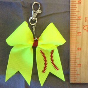 May include: A neon yellow softball bow with a red stitching design, attached to a silver key chain.