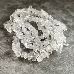 May include: A strand of clear quartz chip beads. The beads are irregular in shape and size, and they are strung together on a clear thread.