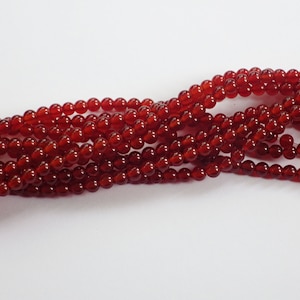 May include: A strand of red carnelian beads. The beads are round and smooth, and they have a glossy finish.