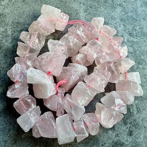 May include: A strand of pink rose quartz beads, each bead is a natural, irregular shape and has been strung together with pink thread.