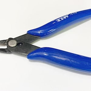 Może przedstawiać: Cążki do drutu z niebieskimi uchwytami i czarnym metalowym ostrzem. Uchwyty mają nadrukowany tekst "X-ACTO 1/70".