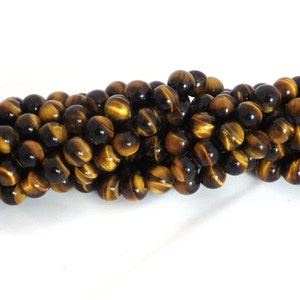 May include: A strand of round tiger's eye gemstone beads featuring a polished finish with alternating bands of golden yellow and dark brown colours. The beads are strung together in a dense, horizontal arrangement, showcasing the natural chatoyancy.