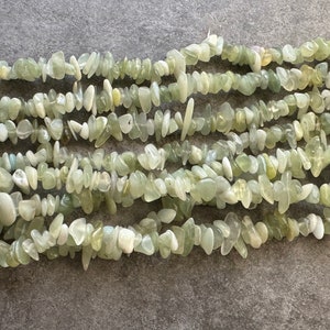 Pu&ograve; includere: Una collezione di frammenti di pietra verde chiaro, traslucidi e opachi, disposti in pi&ugrave; fili orizzontali. I pezzi irregolari e levigati variano per dimensioni e forma, mostrando un mix di tonalit&agrave; menta pallido, salvia e bianco crema.