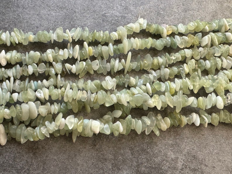 Pu&ograve; includere: Una collezione di frammenti di pietra verde chiaro, traslucidi e opachi, disposti in pi&ugrave; fili orizzontali. I pezzi irregolari e levigati variano per dimensioni e forma, mostrando un mix di tonalit&agrave; menta pallido, salvia e bianco crema.