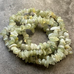 Pu&ograve; includere: Una collana composta da frammenti di pietre preziose verde chiaro disposti in una spirale circolare. Le pietre sono traslucide e variano per forma e dimensione, con superfici levigate e lucide che presentano inclusioni giallo pallido e bianche.