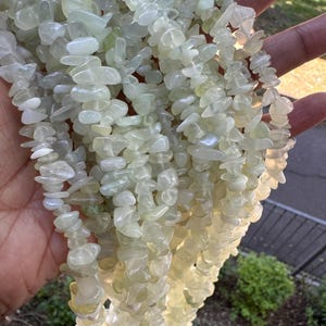 Pu&ograve; includere: Una collezione di molteplici fili di scaglie di pietre preziose levigate, di colore verde pallido e traslucide. Le pietre sono di forma e dimensioni irregolari, con una finitura liscia e lucida che cattura la luce, creando un aspetto morbido.