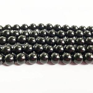 May include: Close-up of multiple rows of shiny, black beads. The beads are round and have a polished surface, reflecting light. They appear to be strung together, possibly for jewellery or craft projects.