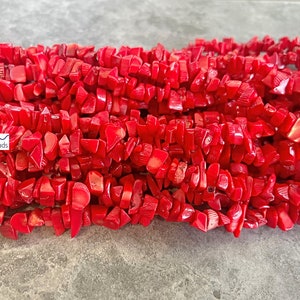 May include: A strand of red coral beads, featuring irregular, chip-shaped beads. The beads are a vibrant red colour and have a natural, organic texture.