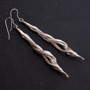 May include: A pair of silver earrings with a twisted, rope-like design. The earrings are long and dangle, with a hook closure.