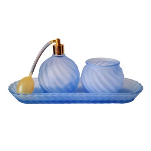 May include: A blue glass tray with a blue glass atomizer bottle and a blue glass jar. The atomizer bottle has a gold top and a clear plastic tube. The tray has a wavy design.