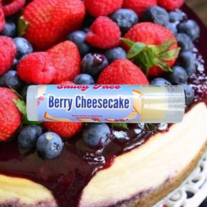 Könnte beinhalten: Eine Lippenbalsam-Tube mit dem Text "Berry Cheesecake" liegt vor einem Käsekuchen, der mit frischen Erdbeeren, Blaubeeren und Himbeeren belegt ist. Der Lippenbalsam ist mit "Saucy Face" beschriftet und wird in Montreal hergestellt.