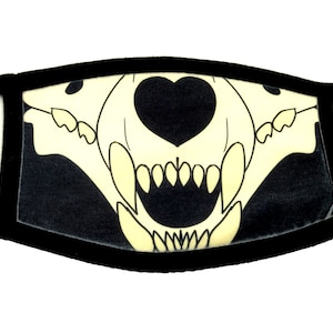 Puede incluir: Máscara de tela negra con un diseño de calavera de animal blanco. La calavera tiene una nariz en forma de corazón y dientes afilados.