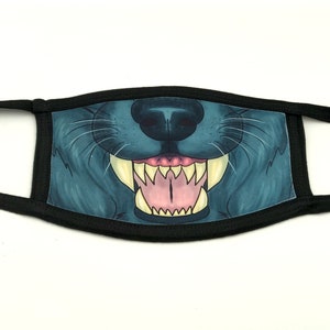 May include: A face mask featuring a detailed illustration of a wolf's mouth, showcasing sharp teeth and a pink tongue. The mask has a black border and ear loops, with a blue and gray color scheme.