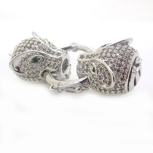 May include: A silver-toned clasp with two panther heads, each with emerald green eyes and covered in clear sparkling stones.