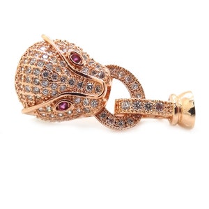 May include: A rose gold-toned animal head charm with clear and red cubic zirconia stones. The charm has a ring and a post for attaching to a bracelet or necklace.