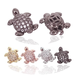 May include: Five turtle charms with clear crystal accents. The charms are in black, gold, silver, rose gold, and black.