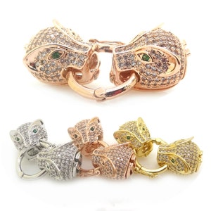 Könnte beinhalten: Ein Satz von vier Tierkopfverschlüssen in Gold, Silber und Roségold. Jeder Verschluss zeigt ein detailliertes Tierkopfdesign mit funkelnden klaren Strasssteinen und grünen Smaragdaugen.