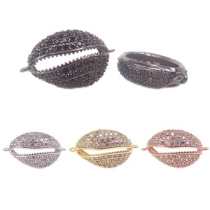 Könnte beinhalten: Drei Paare muschelförmiger Verschlüsse mit einem kristallartigen Design. Die Verschlüsse sind in Schwarz, Silber und Gold erhältlich.