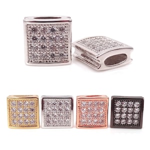 Puede incluir: Cinco cuentas de amuleto de forma cuadrada con un engaste pavé de piedras de circonita cúbica transparentes. Las cuentas se muestran en cinco colores diferentes: oro, plata, oro rosa y negro.