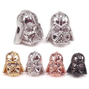 May include: Five Darth Vader head beads in different colours: silver, gold, rose gold, black, and silver with clear rhinestones. The beads are approximately 2.5 cm tall and have a hole at the top for stringing.