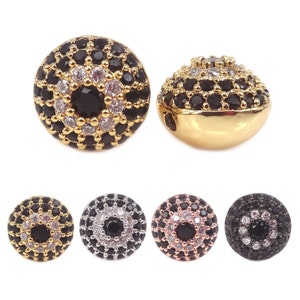 May include: A set of four round beads with a black evil eye design. The beads are surrounded by small white rhinestones and have a gold, silver, rose gold, and black finish.