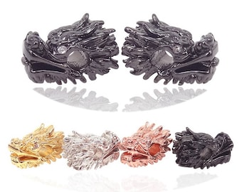 May include: Five dragon head charms in different finishes: gold, silver, black, rose gold, and black. The charms are detailed with textured scales and a small clear rhinestone on each head.
