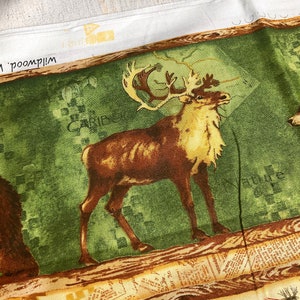 May include: A green and brown fabric with a printed image of a caribou standing on a wooden log. The fabric has a vintage newspaper print design with the word "Caribou" and "Nature" printed on it. There are also images of fishing lures printed on the fabric.