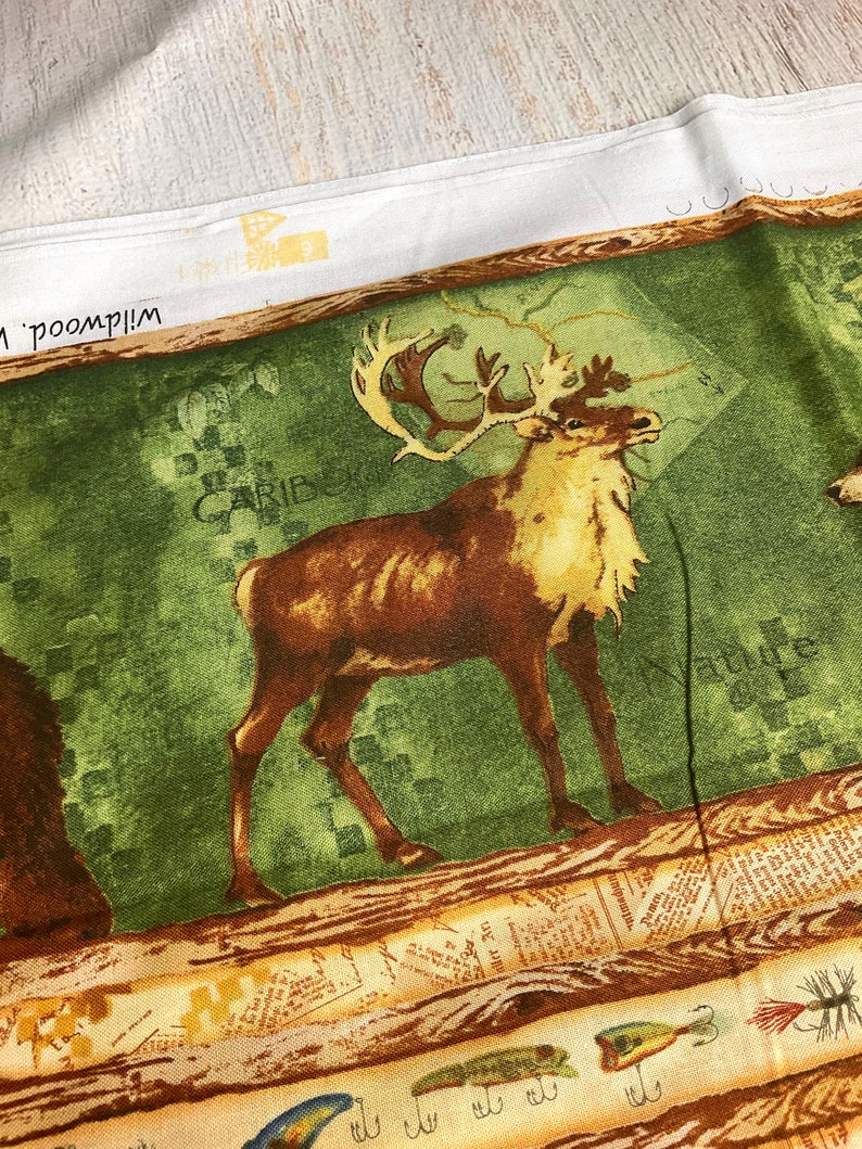 May include: A green and brown fabric with a printed image of a caribou standing on a wooden log. The fabric has a vintage newspaper print design with the word "Caribou" and "Nature" printed on it. There are also images of fishing lures printed on the fabric.