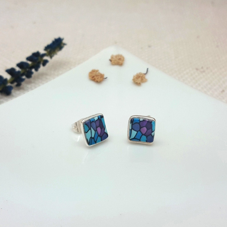 May include: A pair of silver stud earrings with square blue and purple mosaic designs.