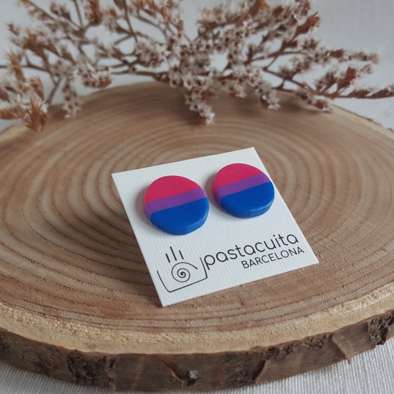 May include: A pair of round, bi-colored earrings with pink, purple, and blue stripes. The earrings are on a white card with the text "pastacuita BARCELONA".