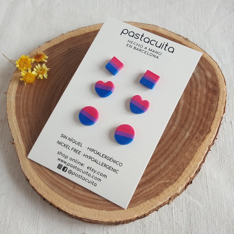 May include: A set of six bi pride earrings, including two hearts, two squares, and two circles. The earrings are made of polymer clay and are nickel-free and hypoallergenic. The earrings are displayed on a white card with the text "pastacuita, HECHO A MANO EN BARCELONA, SIN N&Iacute;QUEL - HIPOALERG&Eacute;NICO, NICKEL FREE - HYPOALLERGENIC, shop online: etsy.com, www.pastacuita.com, @pastacuita".