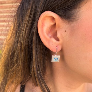 Puede incluir: Pendientes de plata con un peque&ntilde;o dije cuadrado con un dise&ntilde;o geom&eacute;trico azul y naranja.