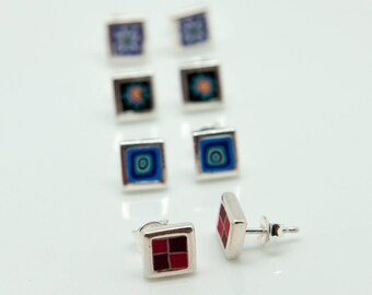 Puede incluir: Un conjunto de pendientes de plata con azulejos cuadrados de colores. Los pendientes tienen una variedad de diseños, que incluyen azul, rojo y naranja.
