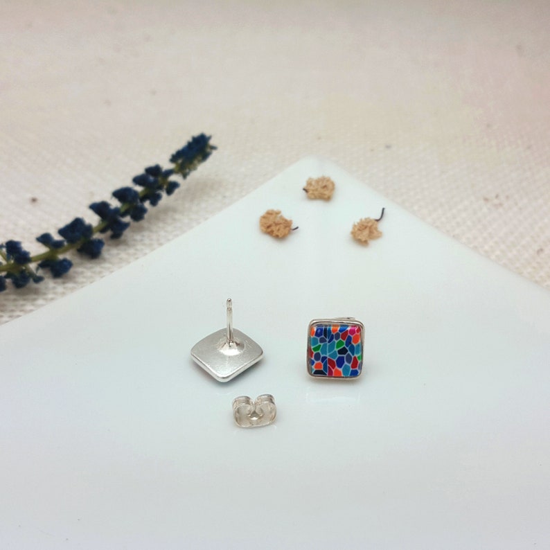 May include: A pair of silver stud earrings with a square-shaped colorful mosaic design. The earrings have a silver post and butterfly backing.