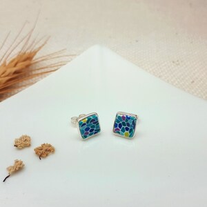 May include: A pair of silver stud earrings with square blue, green, purple, and yellow mosaic-style designs.