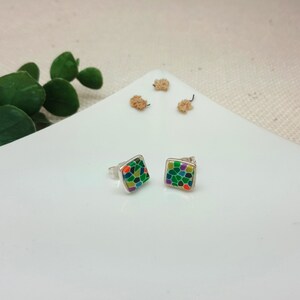May include: A pair of silver stud earrings with square-shaped green, orange, yellow, and purple mosaic designs.