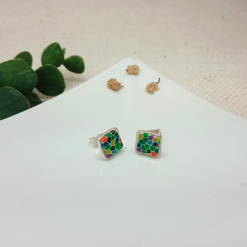May include: A pair of silver stud earrings with square-shaped green, orange, yellow, and purple mosaic designs.