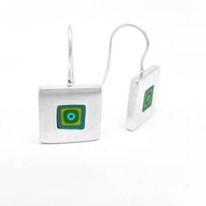 Puede incluir: Pendientes de plata con dise&ntilde;o cuadrado. El cuadrado tiene un cuadrado m&aacute;s peque&ntilde;o en el interior con un patr&oacute;n de c&iacute;rculo conc&eacute;ntrico en tonos de verde, azul y amarillo.