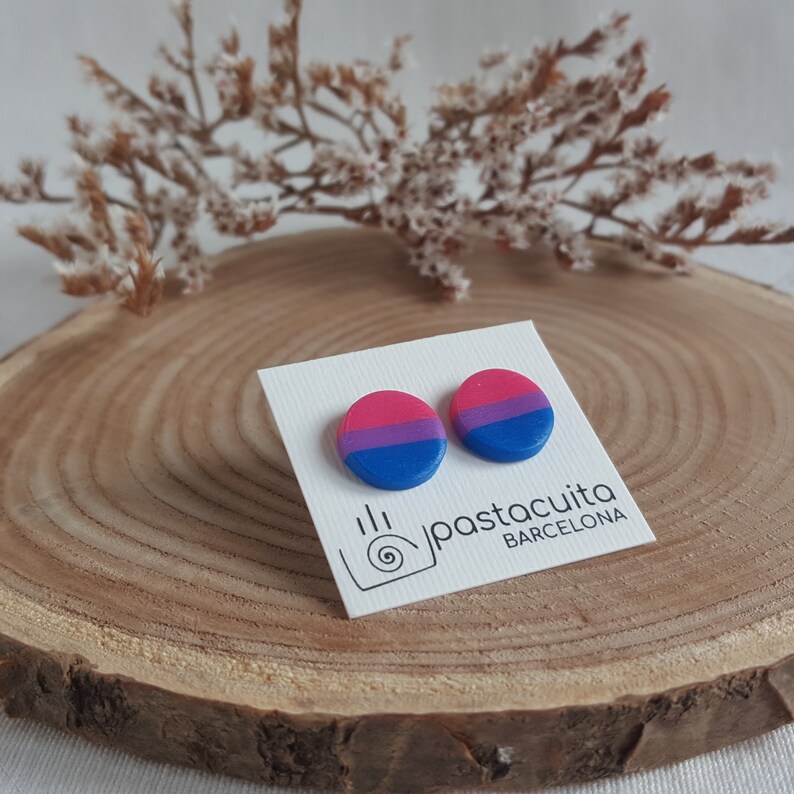 May include: A pair of round, bi-colored stud earrings with pink, white, and blue stripes. The earrings are displayed on a white card with the text "pastacuita BARCELONA".