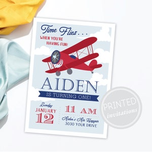 May include: A red and blue airplane birthday invitation for a boy named Aiden turning one. The invitation features a red biplane flying in a blue sky with white clouds. The text "Time Flies... When You're Having Fun!" is at the top of the invitation. The invitation also includes the date and time of the party, "Sunday, January 12, 11 AM", and the location, "Aiden's Air Hangar, 3030 Your Drive".