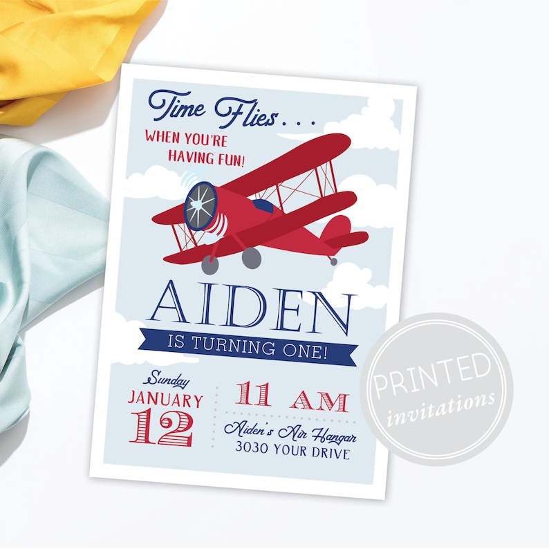 May include: A red and blue airplane birthday invitation for a boy named Aiden turning one. The invitation features a red biplane flying in a blue sky with white clouds. The text "Time Flies... When You're Having Fun!" is at the top of the invitation. The invitation also includes the date and time of the party, "Sunday, January 12, 11 AM", and the location, "Aiden's Air Hangar, 3030 Your Drive".