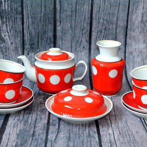 May include: A tea set featuring a teapot, a lidded sugar bowl, a creamer, and four cups with matching saucers. Each piece is bright orange with large white polka dots, a white interior, and a thin gold rim along the edges of the ceramic vessels.